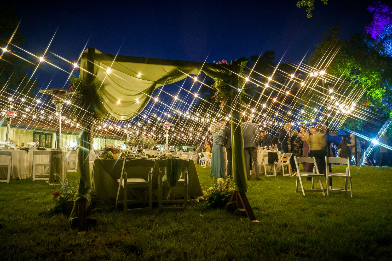 Outdoor wedding reception tent illuminated with twinkling string lights and lanterns creating a magical evening ambiance.