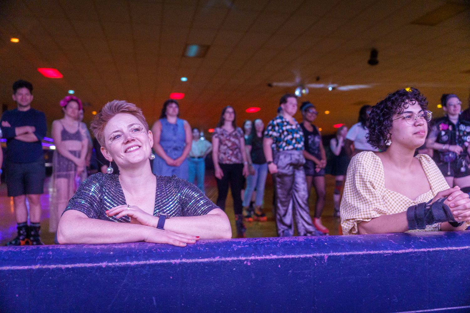 Crowd of people in a dimly lit auditorium with purple and blue lighting creating a festive atmosphere.
