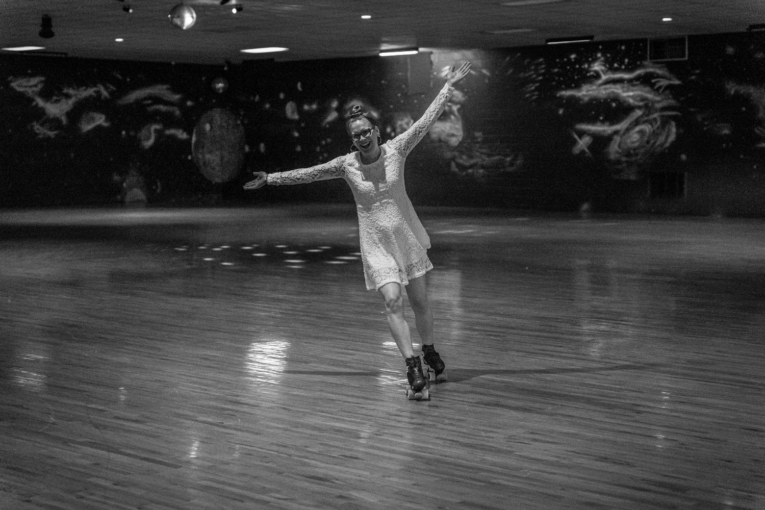 A figure skater performs gracefully in an indoor rink, captured in black and white with dramatic lighting.