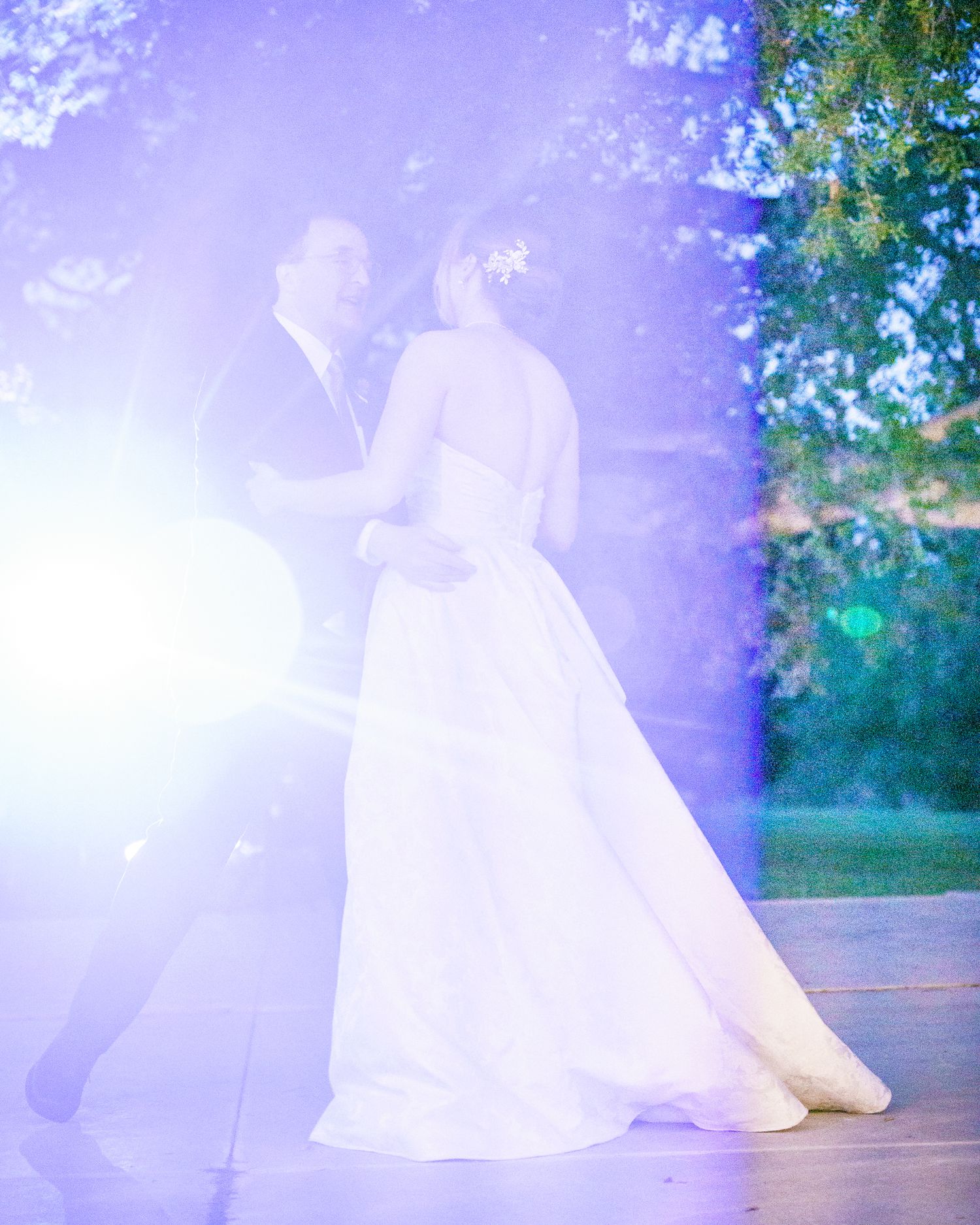 A dreamy wedding photo showing figures dancing in ethereal light and fog while surrounded by greenery.