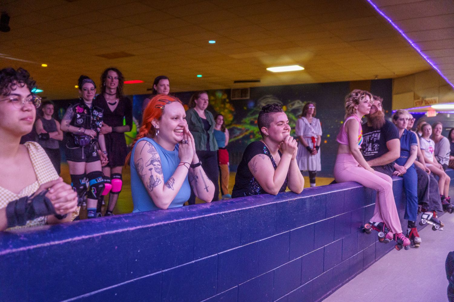 A crowd of spectators reacts emotionally while watching a performance in a dimly lit venue with purple lighting.
