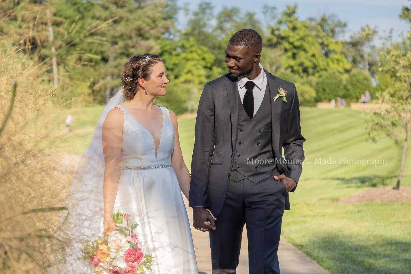 Wedding couple walks together on manicured lawn during outdoor ceremony.