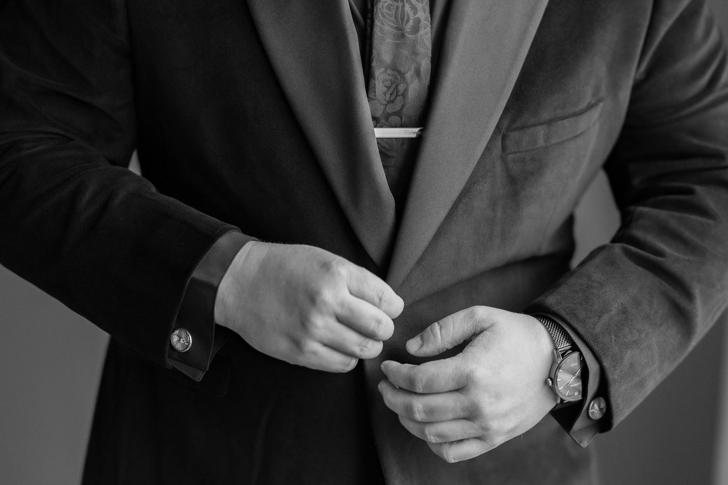 Close-up of groom adjusting his suit jacket buttons.