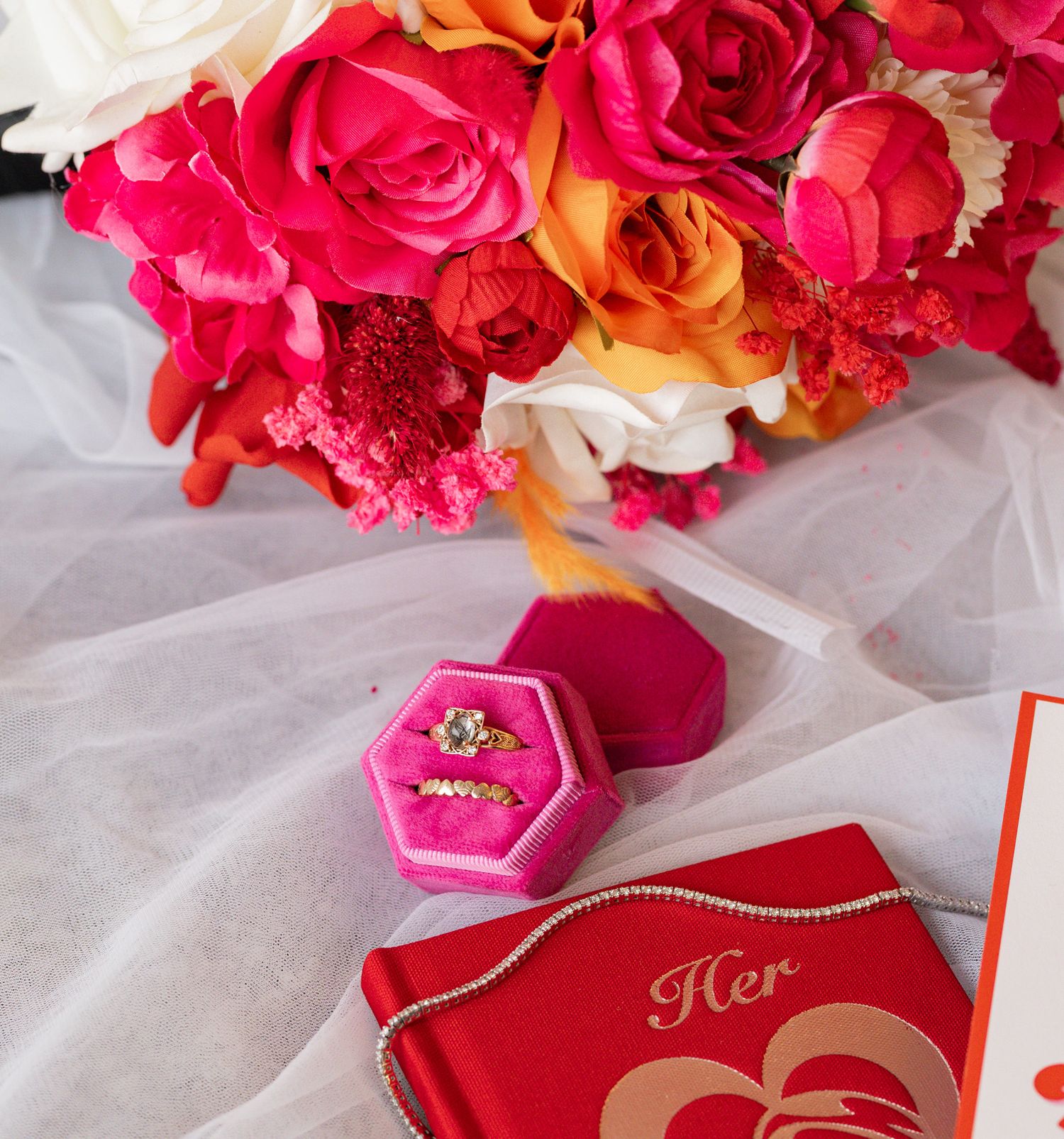 Wedding details with vibrant roses and pink velvet ring box on white tulle fabric.