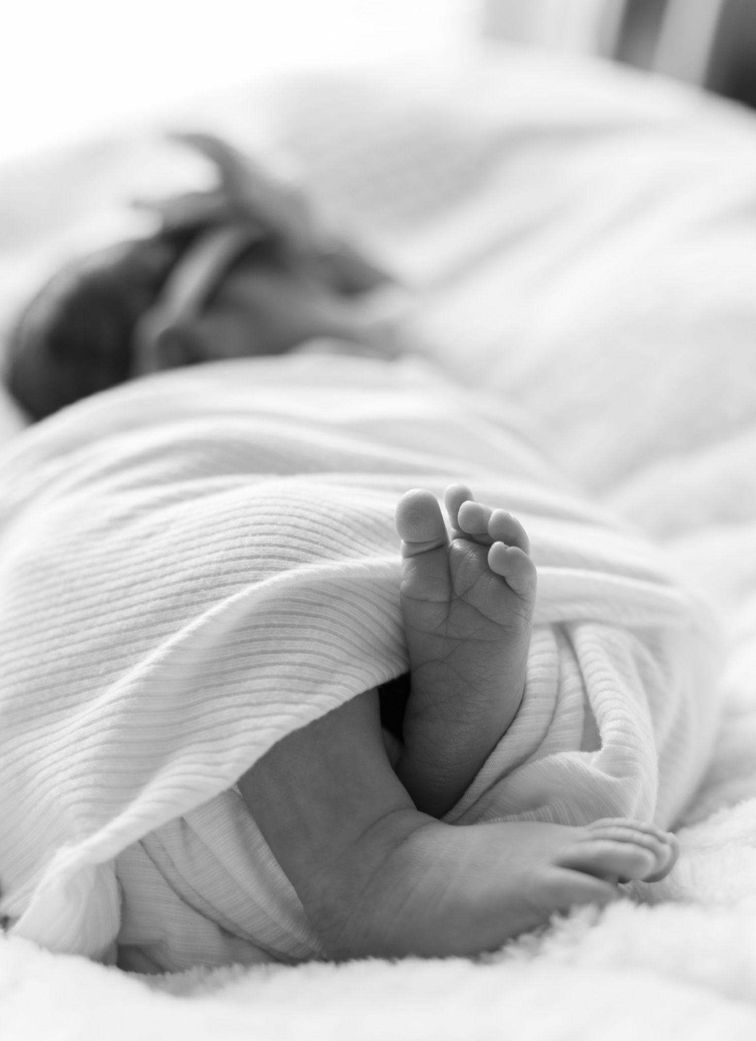 Close-up black and white photo of baby's foot wrapped in soft white blanket.