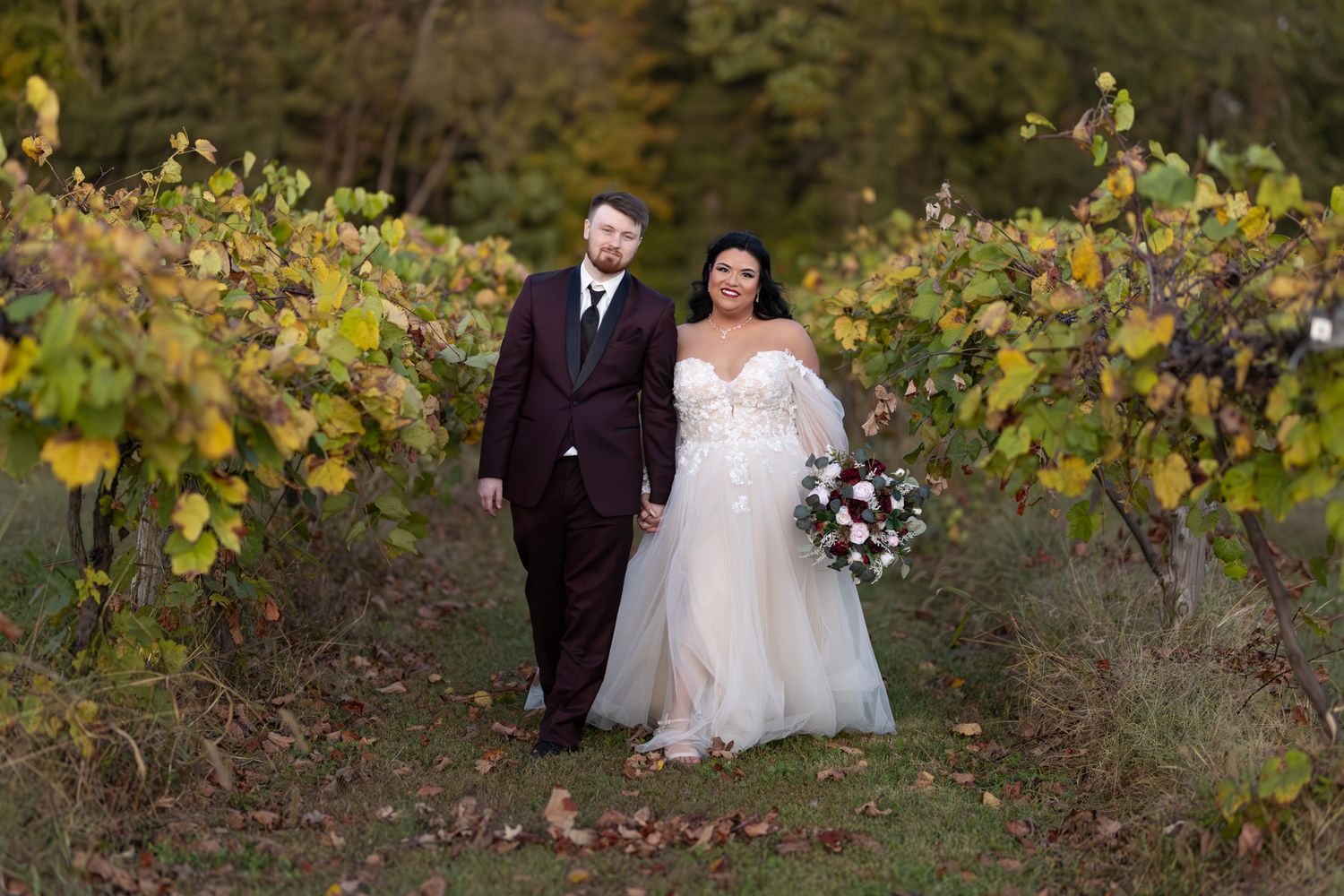 A couple walk hand in hand through a scenic vineyard on their wedding day.