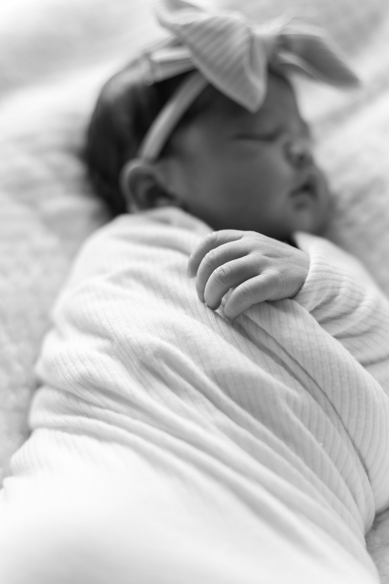 Artistic black and white photo of sleeping infant with bow headband.