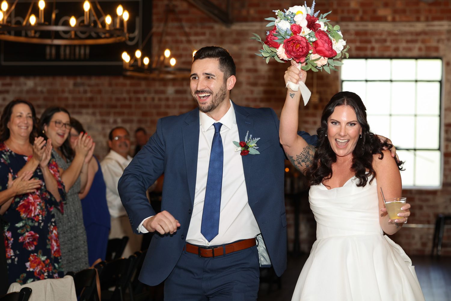 Celebrating newlyweds exit their wedding ceremony while guests cheer in rustic brick venue.