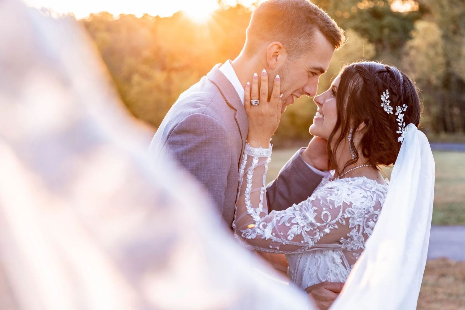 A tender romantic moment between newlyweds during sunset with a bride in lace gown and flowing veil.