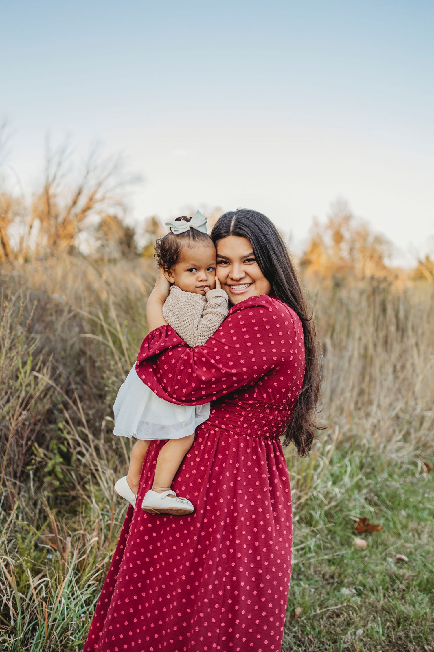 A tender outdoor scene showing affection between two people wearing a red polka dot dress and gray outfit in a field at sunset.