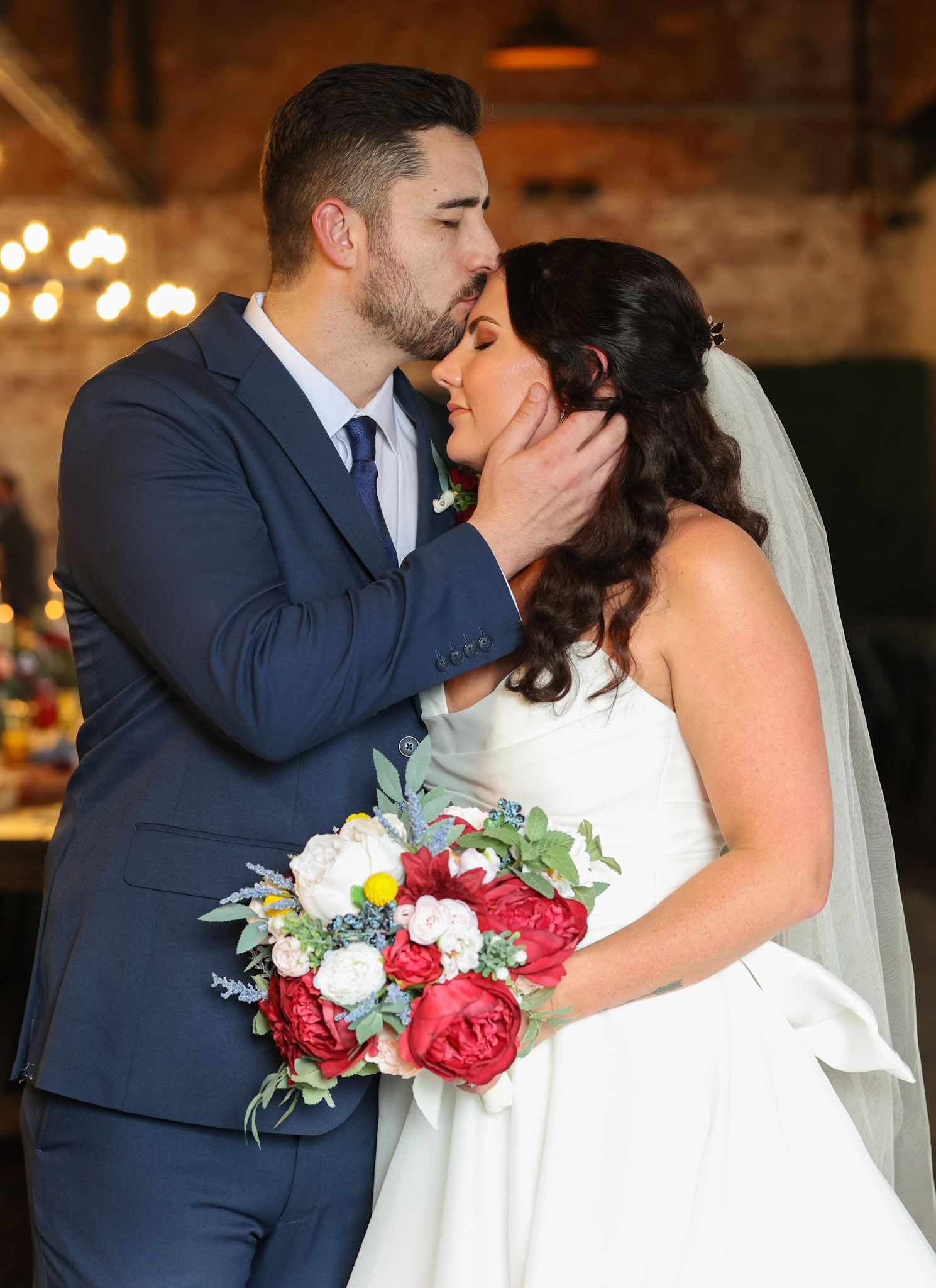 Tender wedding portrait of couple embracing with red rose bouquet.