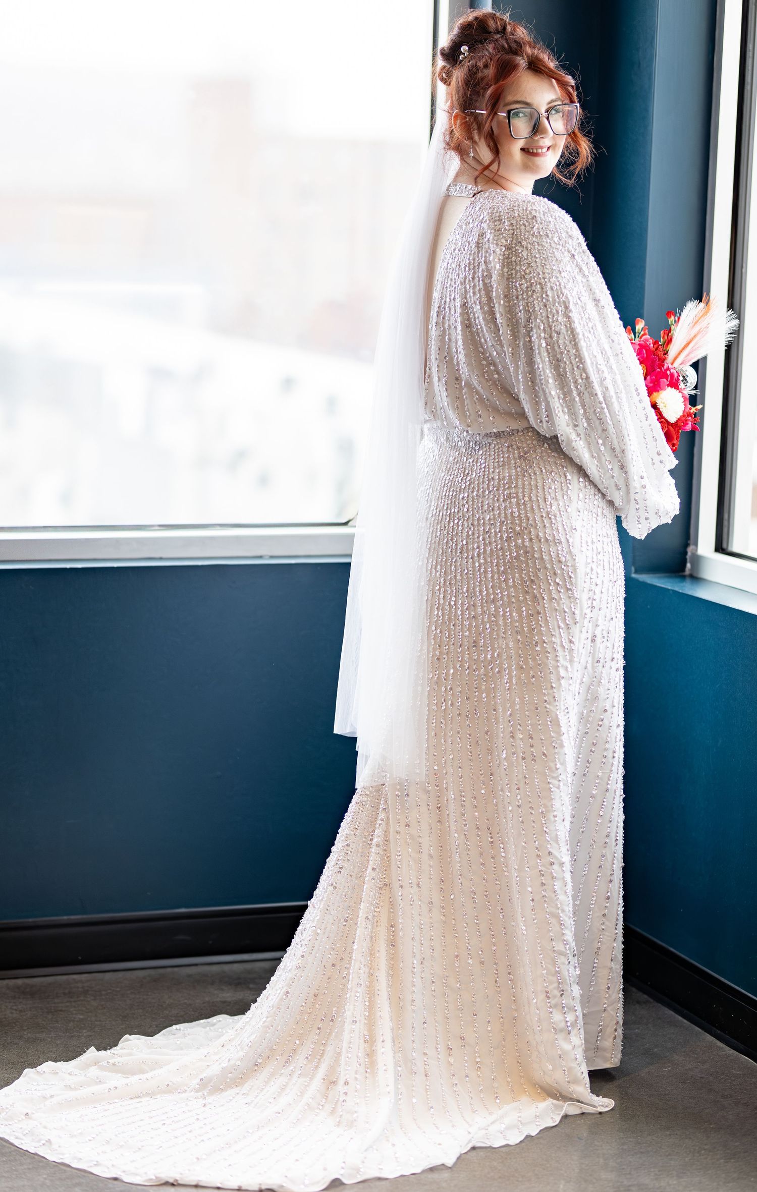 Wedding dress with flowing lace sleeves and sequins photographed in front of window.