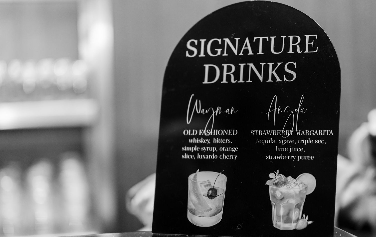 Black and white signage displaying signature cocktail menu options at a wedding reception.