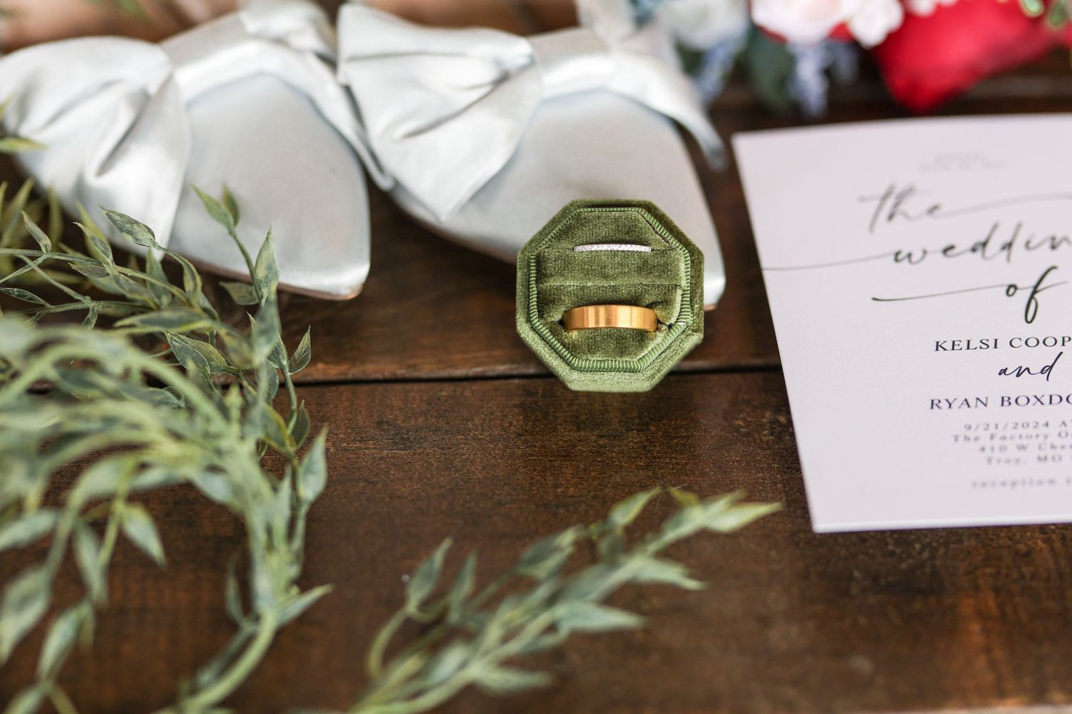 Wedding rings nestled in octagonal box with greenery and invitation.