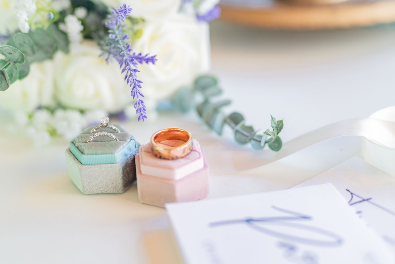 Wedding ring boxes and floral decorations arranged on a light surface with lavender accents.