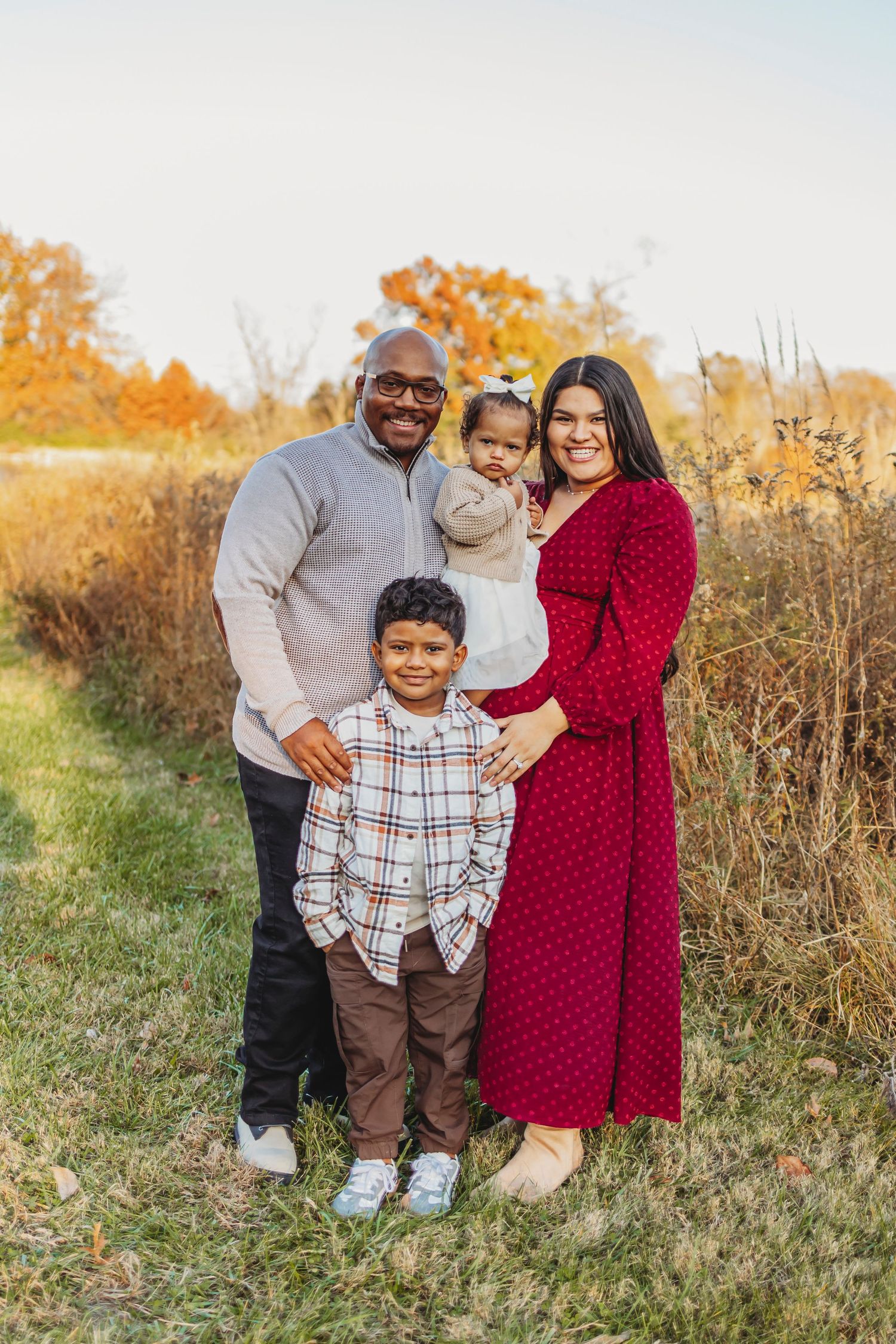 Family in fall outfits enjoying an outdoor photoshoot in golden autumn field with tall grass and warm lighting.