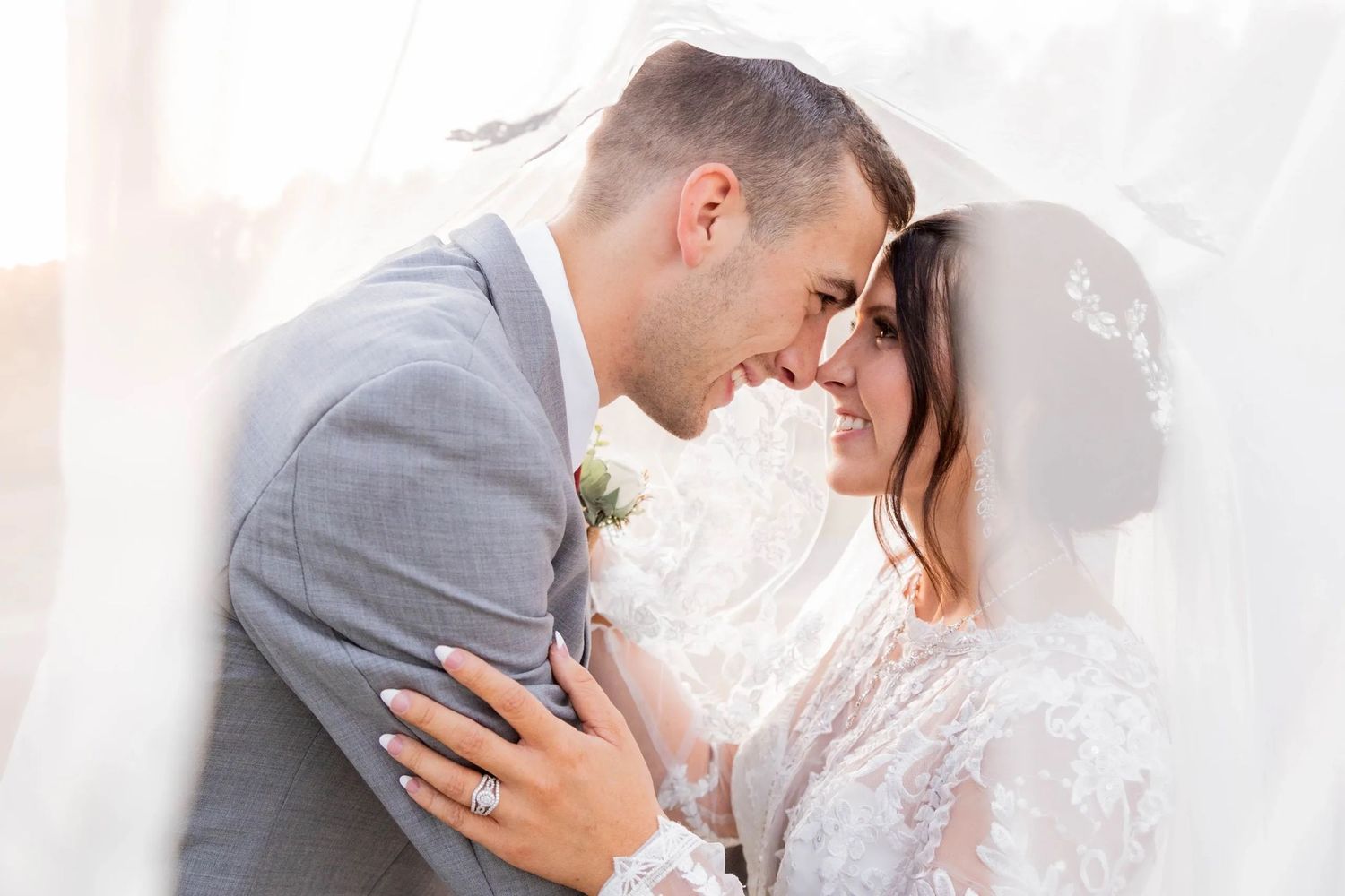 Intimate romantic moment between newlyweds under sheer white veil.
