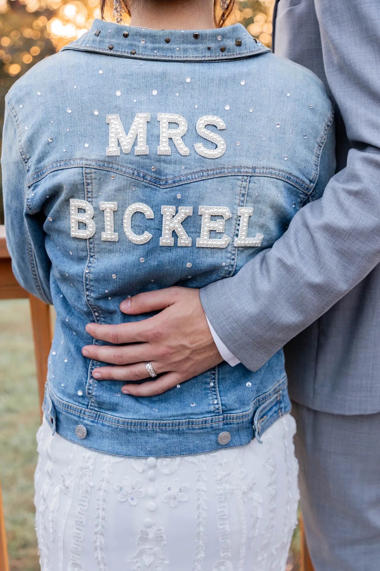 A close-up of a custom denim jacket with 'MRS BICKEL' lettering worn by a bride.