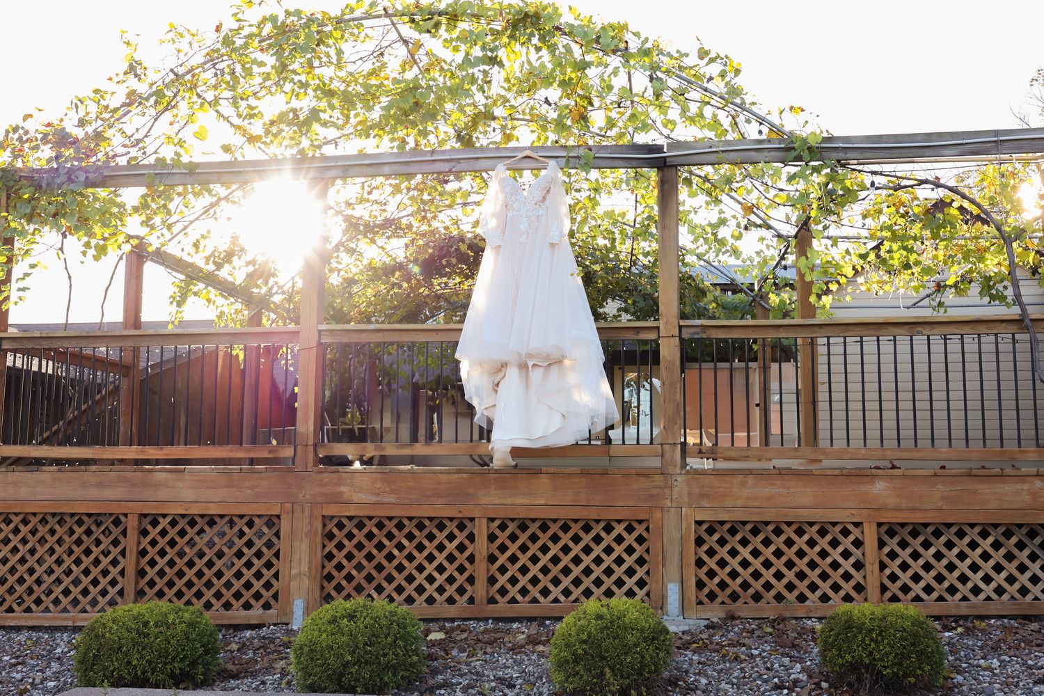 White wedding dress hanging on wooden deck railing at sunset.