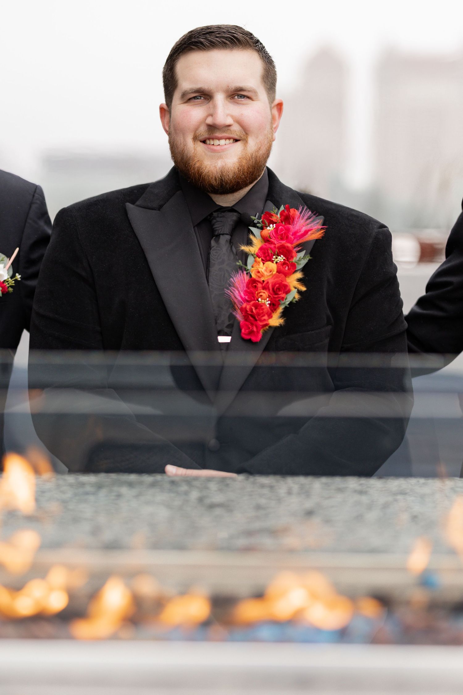 Groom in black suit with bright pink and orange boutonniere smiling.
