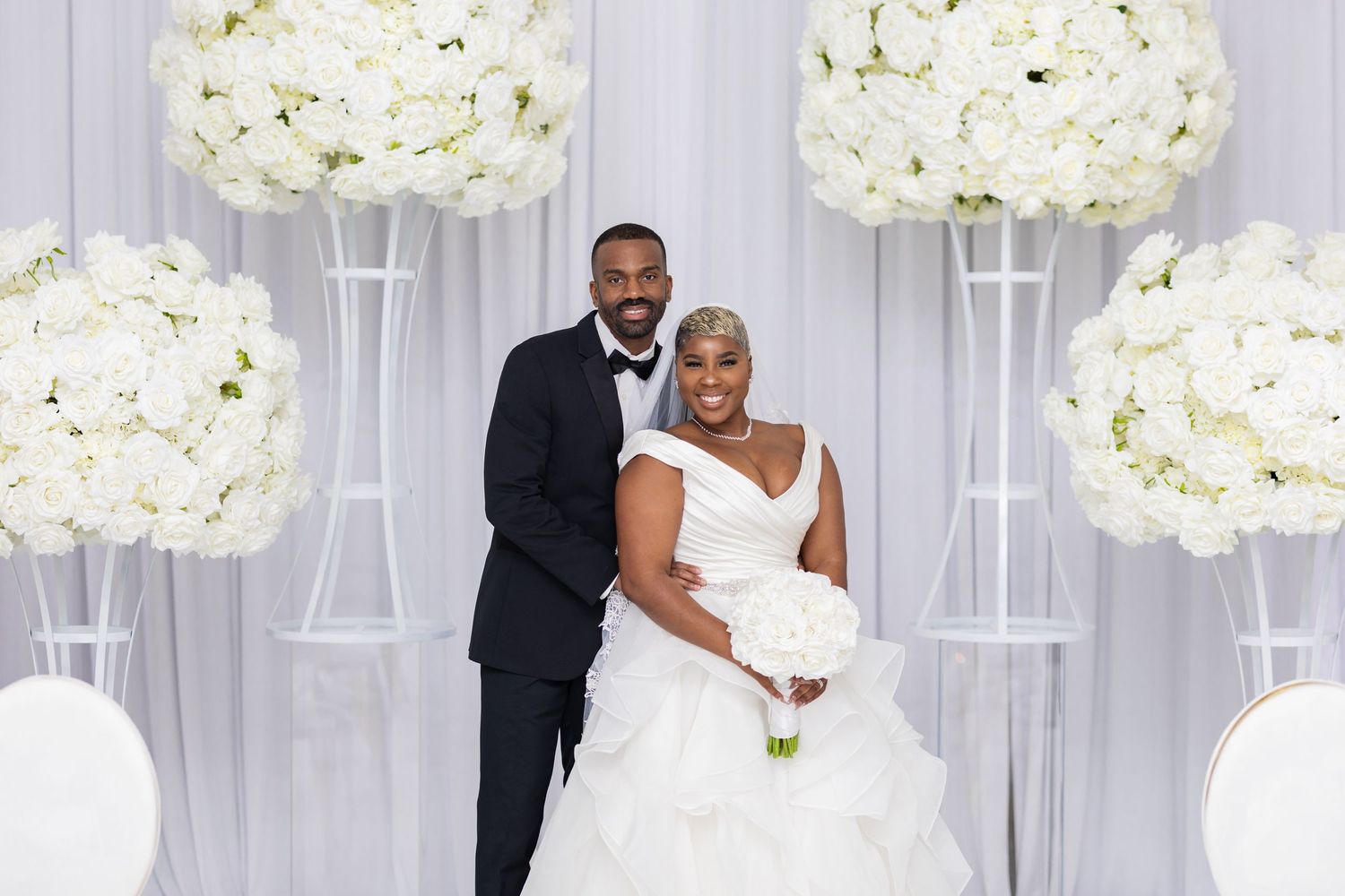 A wedding portrait setup with elegant white floral arrangements and drapery creating a luxurious backdrop.