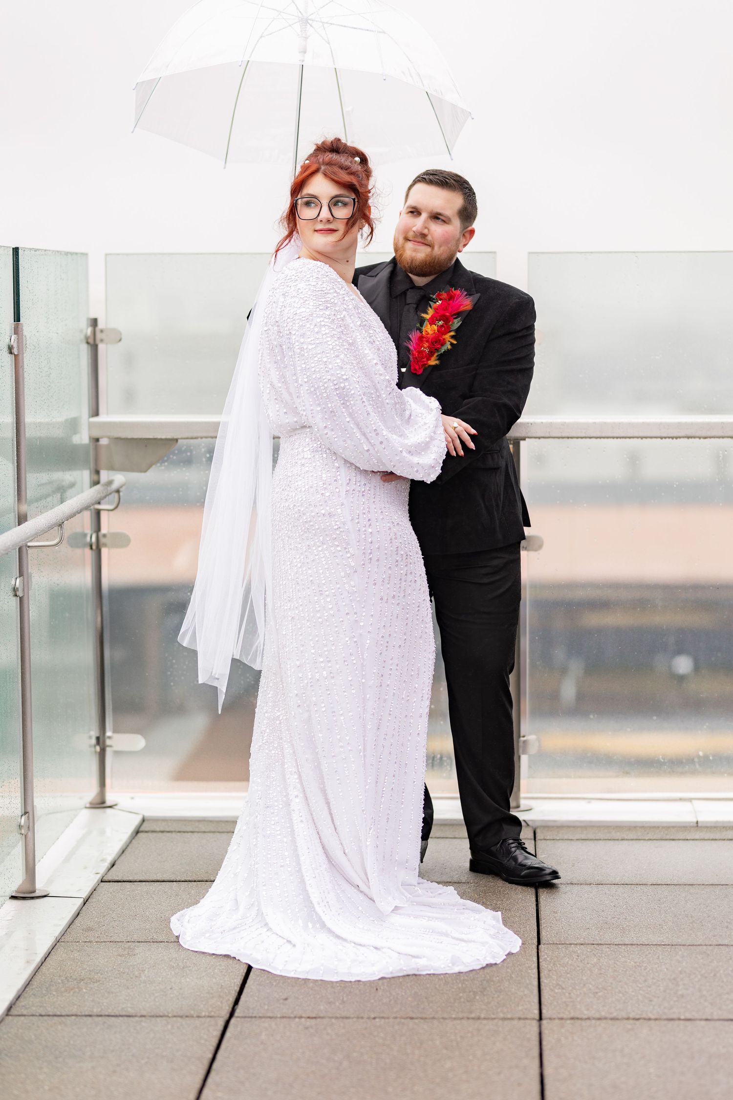 Couple embraces under clear umbrella during rooftop wedding photoshoot.