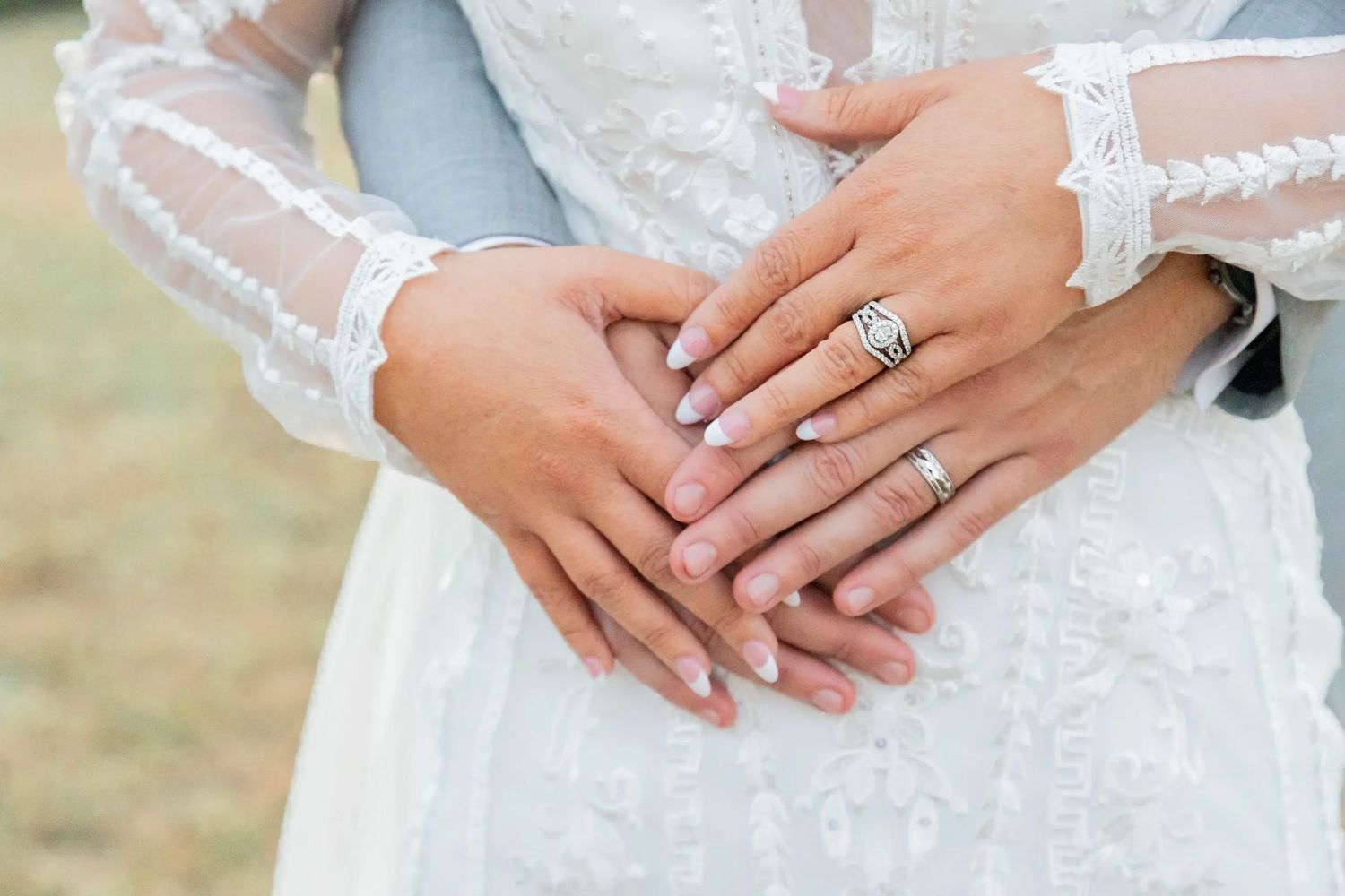 Close-up of newlyweds' hands with wedding ring on lace wedding dress.