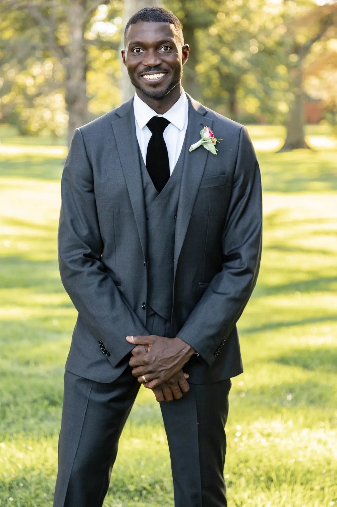 A series of five images showing a person in a dark formal suit posing outdoors in a sunlit garden setting.
