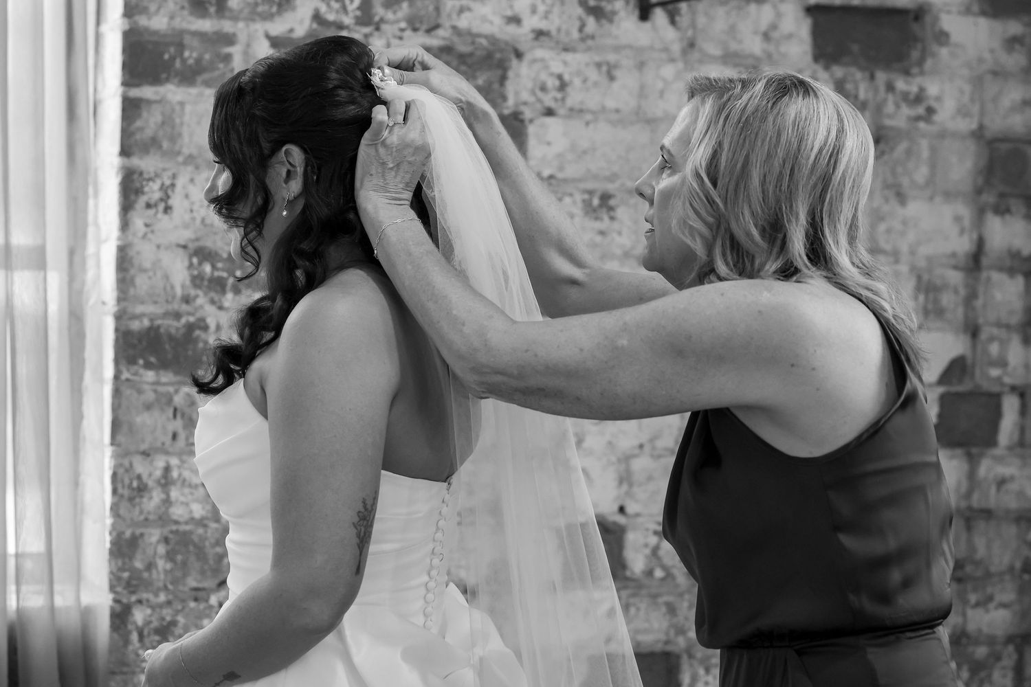 Black and white photo of helping hands arranging wedding veil.
