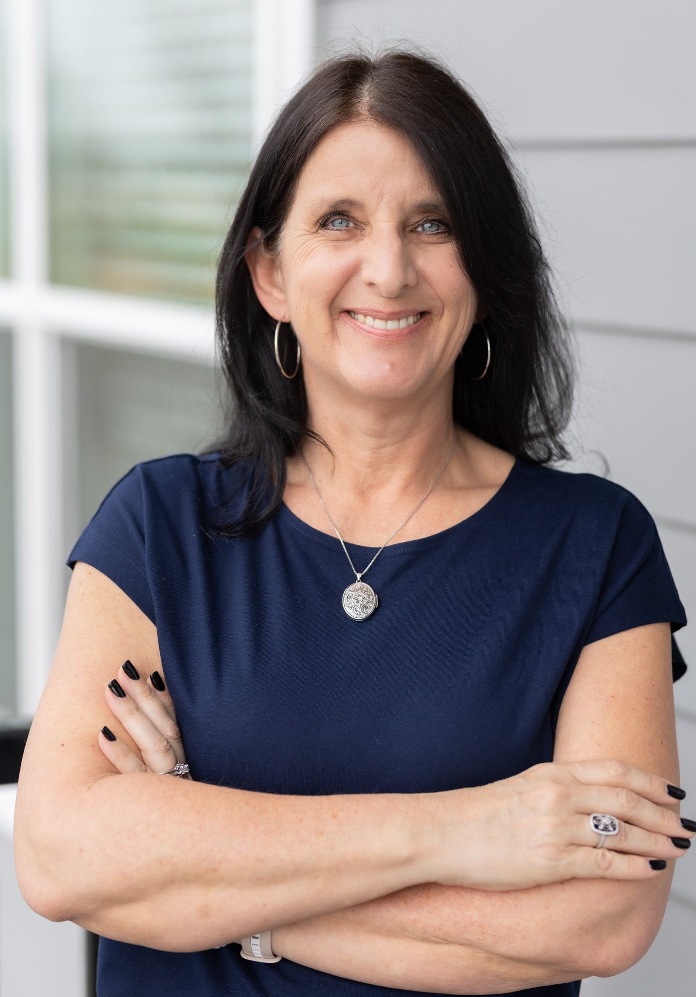 Professional headshot of woman in navy blue top with silver necklace.