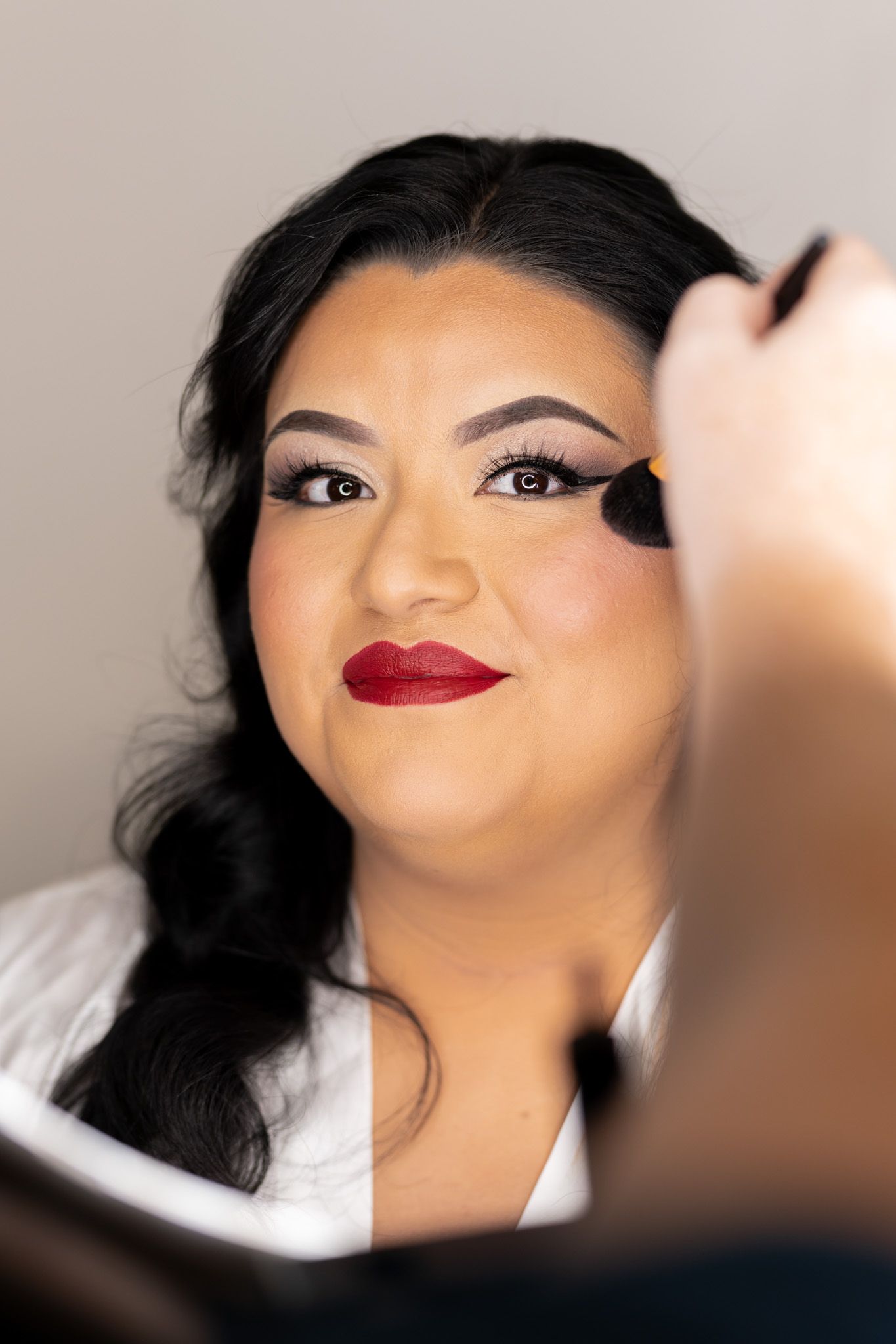Makeup artist applies eyeshadow with brush while model wears classic red lipstick and white blouse.