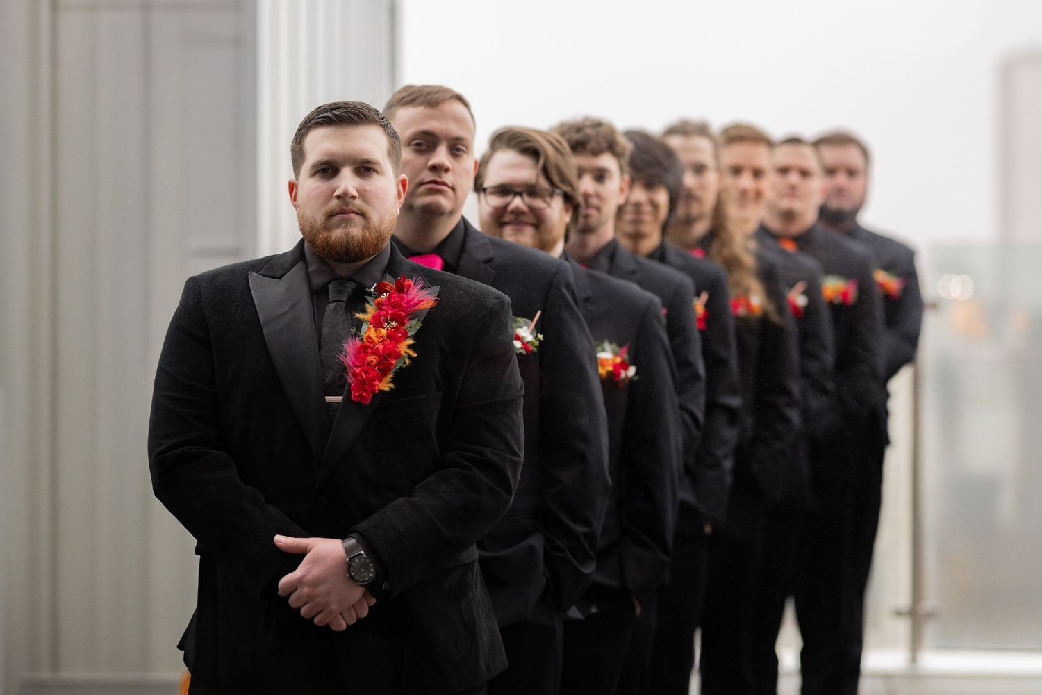 Groomsmen in black suits with red boutonnieres lined up in formal wedding photo.