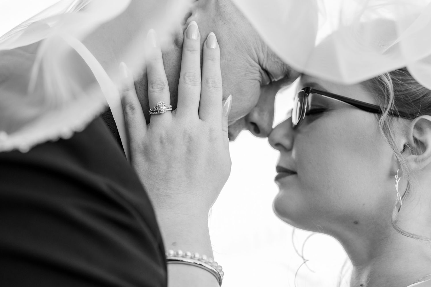 Black and white close-up of tender moment between bride and groom showing wedding rings.