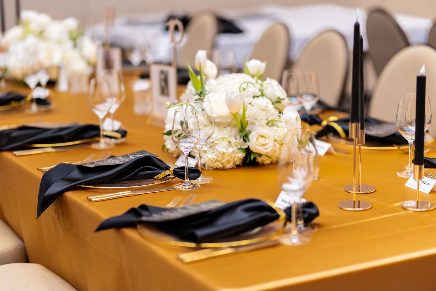 Elegant wedding reception table with gold tablecloth, black napkins and white floral centerpieces.