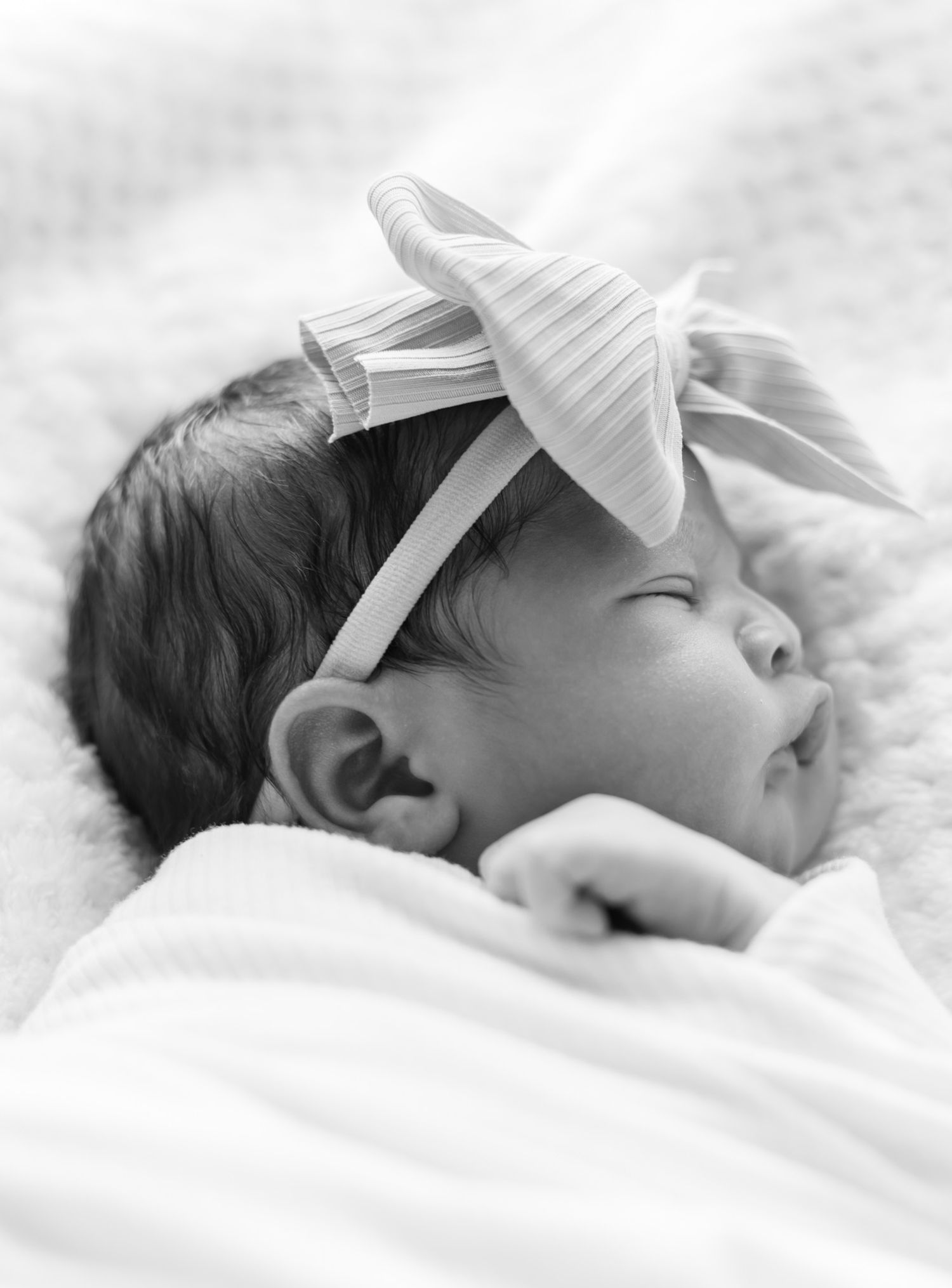 Sleeping newborn wearing white bow headband in black and white portrait.