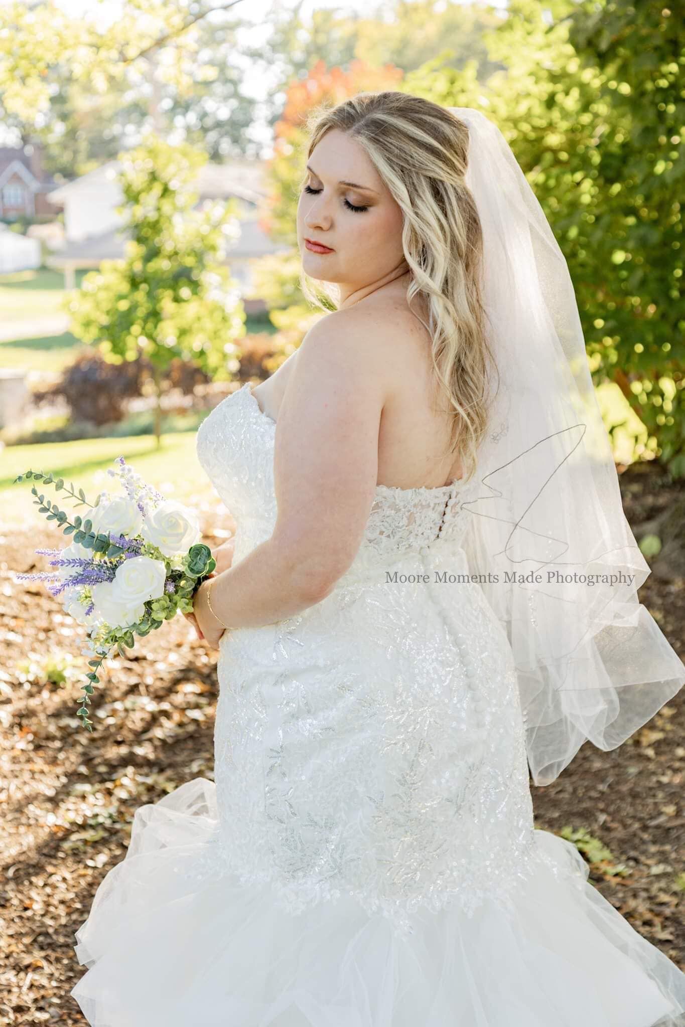Bride in lace wedding dress poses outdoors among autumn foliage.