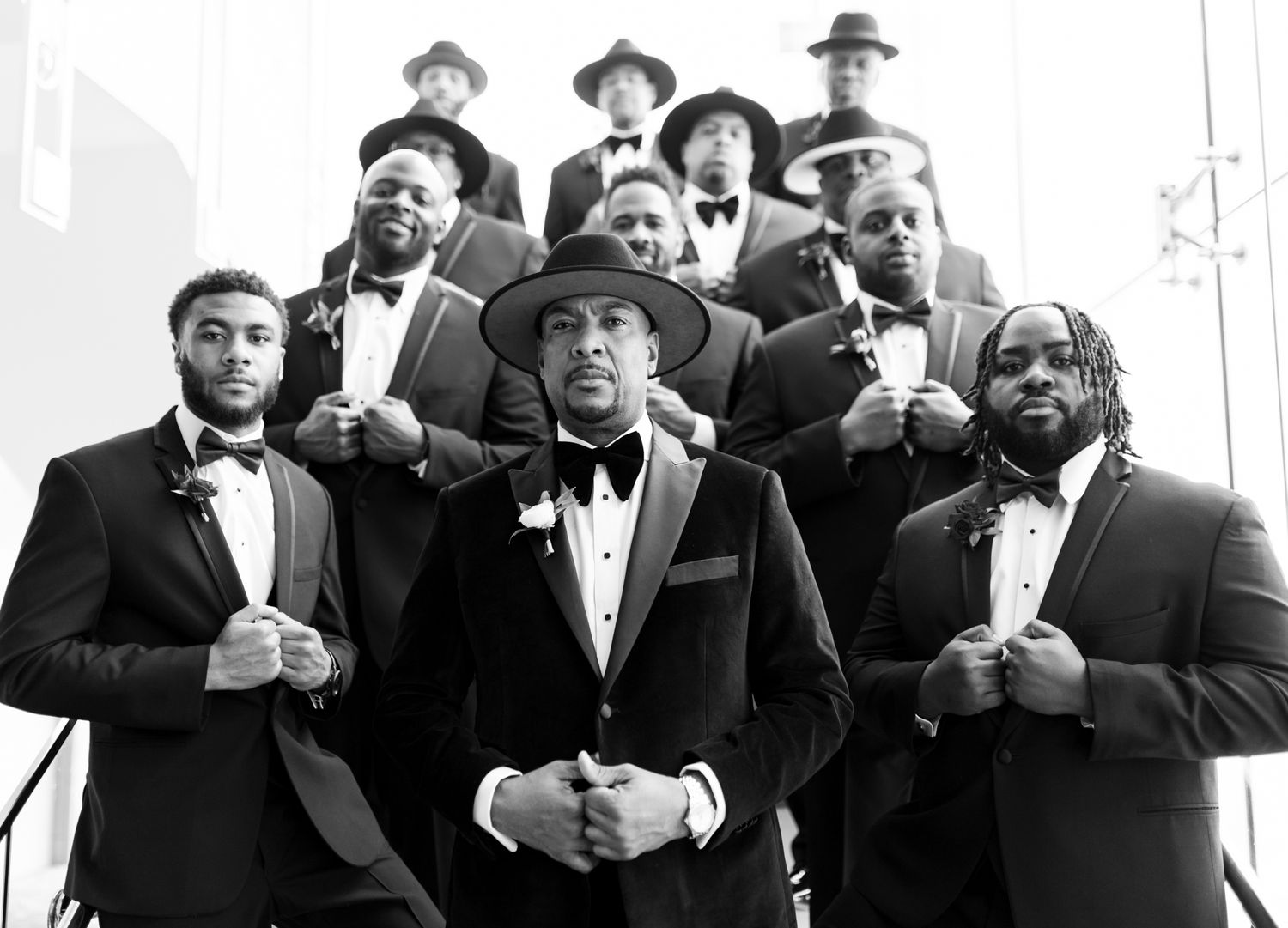 Stylish group of performers with hats and bowties pose together for a black and white photo.