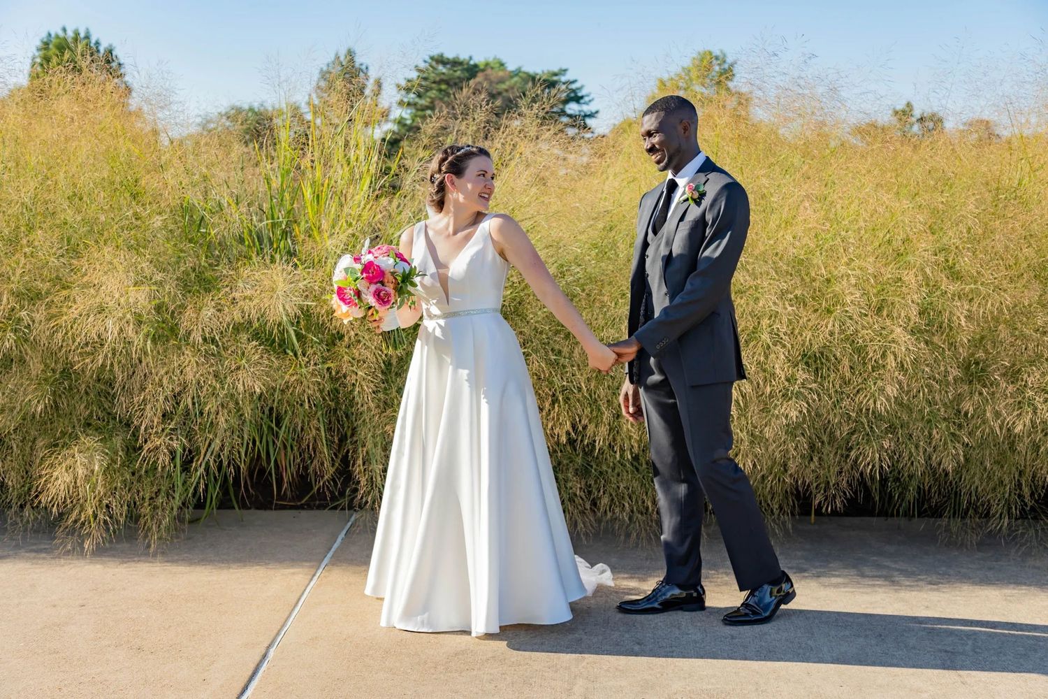A loving couple celebrate their wedding day together on a paved walkway with golden grass in the background.