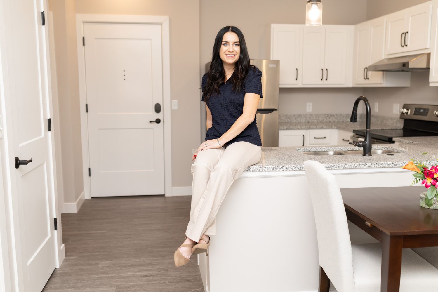 Woman sitting casually on kitchen counter in modern white kitchen interior.