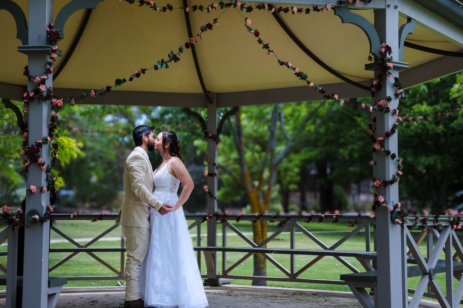 A romantic moment under a gazebo decorated with twinkle lights in a peaceful garden setting.