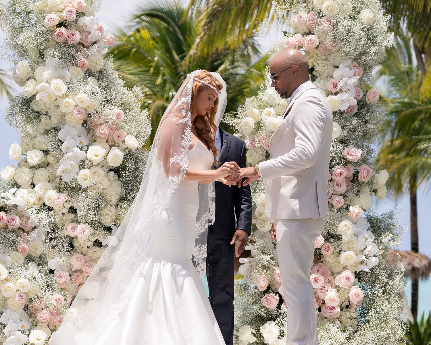 A beautiful outdoor wedding ceremony with guests in white attire and a luxurious floral arch backdrop.