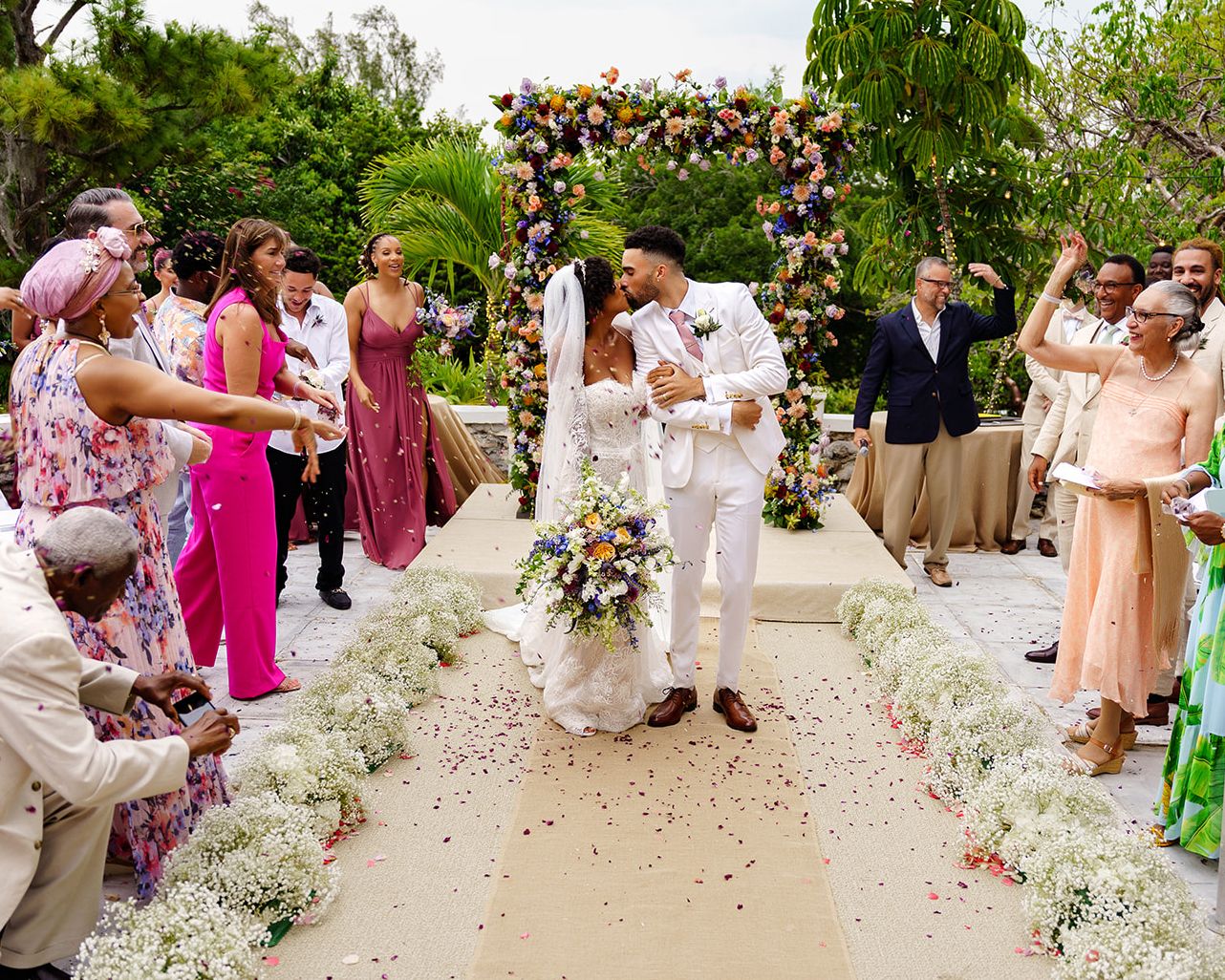 Outdoor wedding ceremony under floral arch with guests gathered on both sides during beautiful garden celebration.