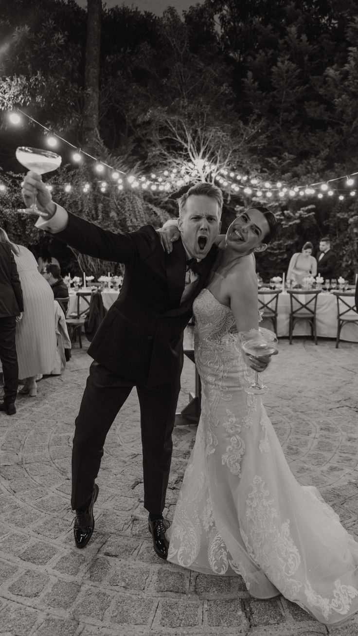 A joyful celebration at an outdoor wedding reception with string lights overhead and a stone patio dance floor.