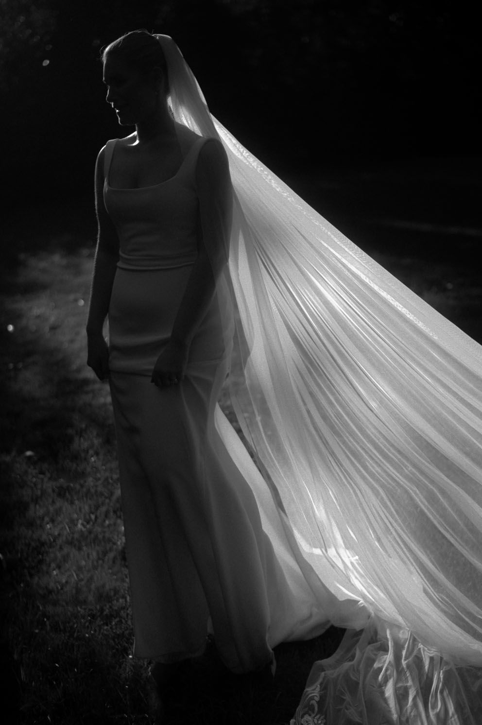 Black and white photo of a bride in a sleek dress with flowing long veil blowing in the wind during an outdoor shoot.