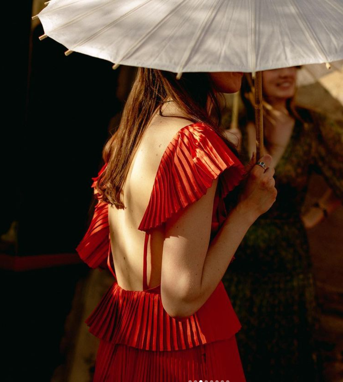 Woman in a red dress poses with a white parasol creating an artistic silhouette effect against a dark background.