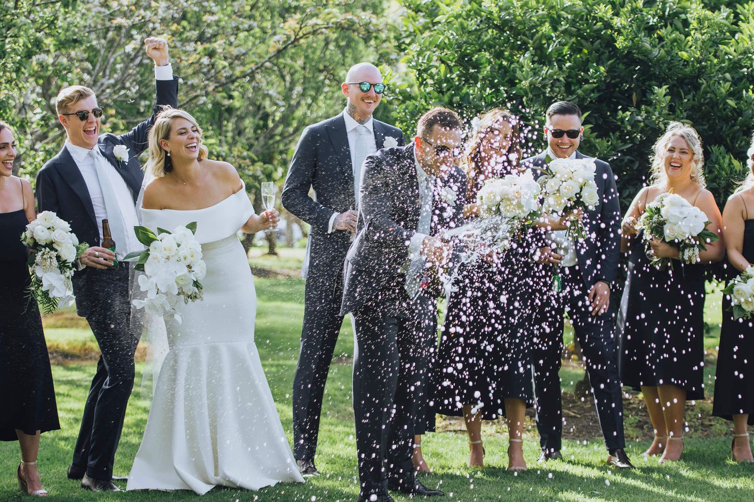 Bridal party celebrating while groom pops open champagne bottle and it sprays everywhere - Zara King Photography, Sydney Australia