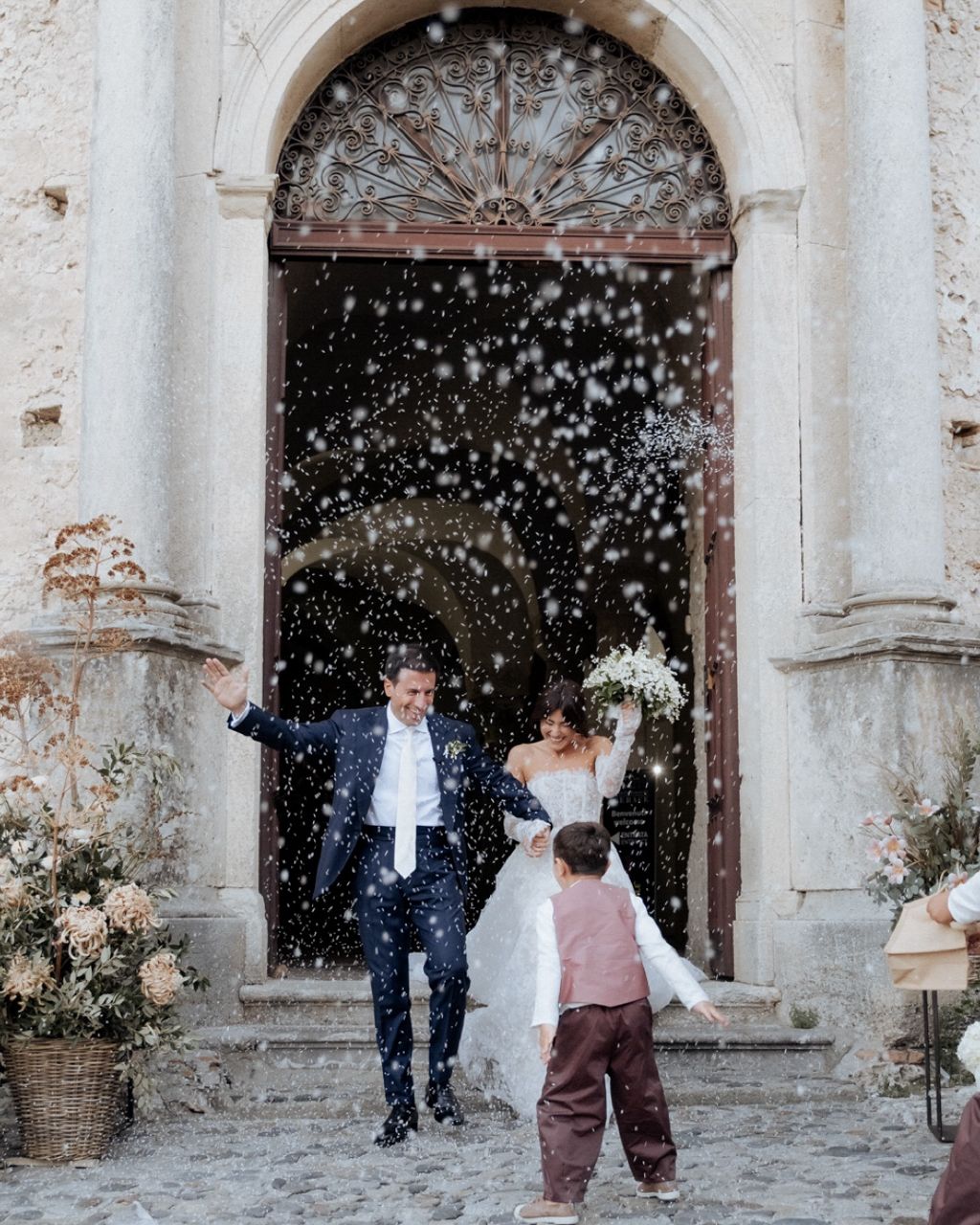 Wedding couple celebrating with confetti shower in front of historic stone church entrance.