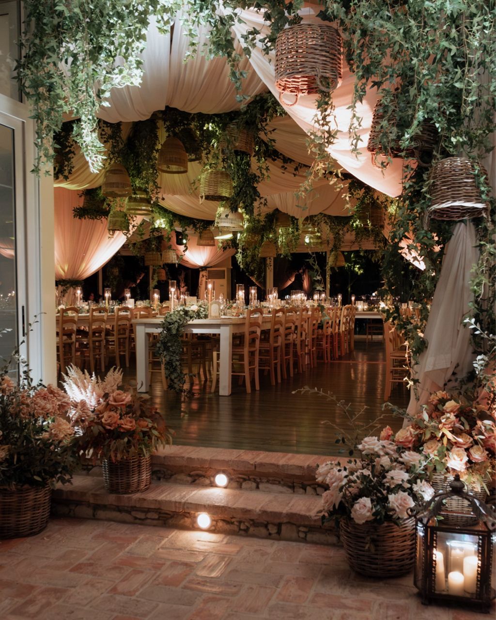 Romantic wedding reception venue decorated with hanging greenery, lanterns, and soft lighting creating an enchanting atmosphere.