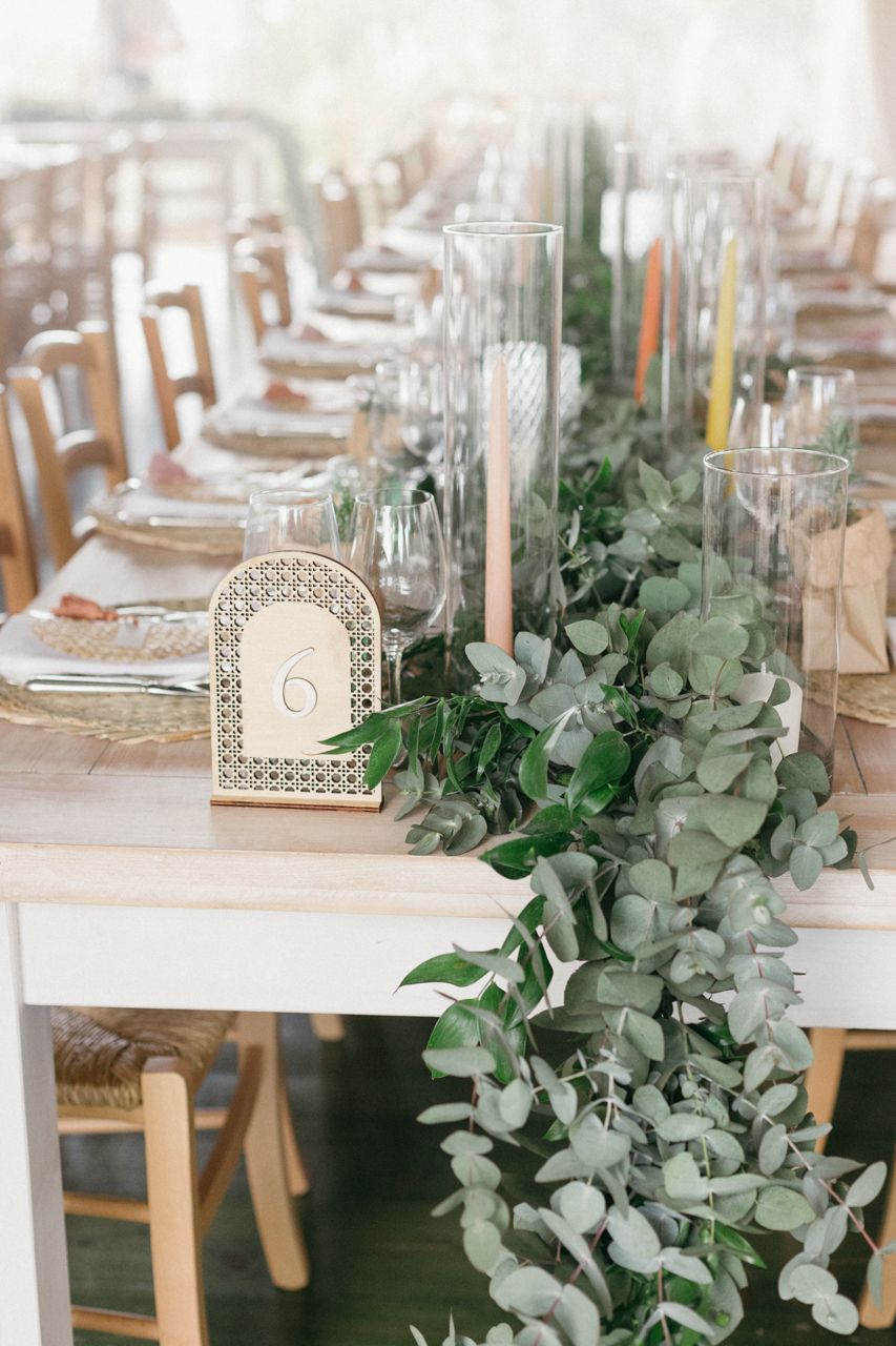 Elegant wedding table setting with eucalyptus garland runner and glass candleholders.