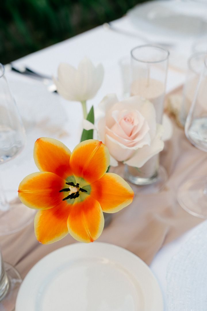 Orange lily and blush rose centerpiece with glassware on an elegant table setting.